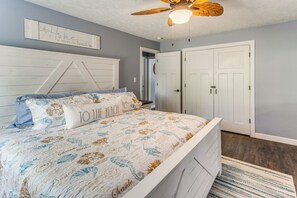 Ein Schlafzimmer mit einem Bett, einem Deckenventilator, einer Tür und einer Wand mit einem dekorativen Schild.