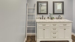 Un baño con tocador blanco, dos espejos, escalera blanca y encimera de mármol.