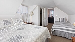 Ein Schlafzimmer mit zwei Betten, einem Fenster mit Jalousien, einer Lampe und einer Tür zu einem anderen Raum.