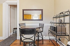 A dining area with a round table, four chairs, a mirror above the table, and a metal shelf with a microwave.