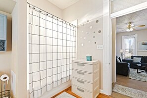 A bathroom with a grid-patterned shower curtain, a white storage unit with drawers, and a visible toilet.