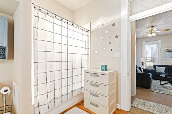 Une salle de bain avec un rideau de douche à motifs géométriques, un meuble de rangement blanc doté de tiroirs et des toilettes bien visibles.