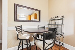 A dining area with a round table, four chairs, a mirror, and a metal rack with kitchen items.