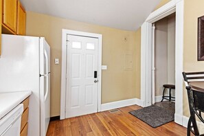 A kitchen with a white refrigerator, wooden cabinets, a white door, and a dining area with a table and chairs.