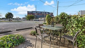 Ein Sitzbereich im Freien mit Tisch und Stühlen, einer Hecke und einem Gebäude im Hintergrund.