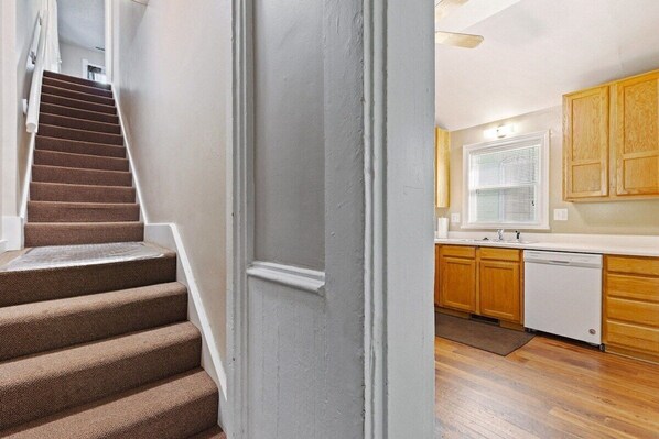A staircase leading to a kitchen with wooden cabinets and a dishwasher.