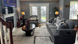 A living room with a grey sofa, a coffee table, a fireplace, and a television on the wall. - Charming 2-bedroom townhome with game room, WiFi, AC, only 10 min to Dollywood. (Sevierville)
