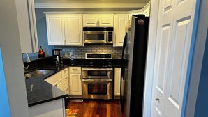 A kitchen with white cabinets, stainless steel appliances, and a wooden floor. - Charming 2-bedroom townhome with game room, WiFi, AC, only 10 min to Dollywood. (Sevierville)