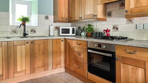 A kitchen with wooden cabinets, a microwave, a stove, and a dishwasher. - 2 bedroom accommodation in Tylorstown (Tylorstown)