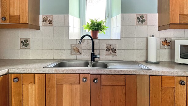 A kitchen with wooden cabinets, a double sink, and a window with a potted plant. - 2 bedroom accommodation in Tylorstown (Tylorstown)