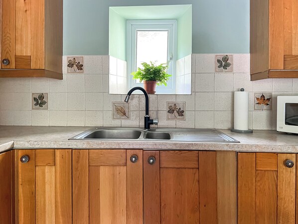 A kitchen with wooden cabinets, a double sink, and a window with a potted plant.