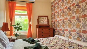 A neatly made bed with a colorful quilt, a wooden dresser, and a window with orange curtains. - 2 bedroom accommodation in Tylorstown (Tylorstown)