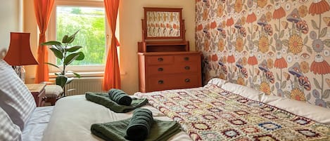 Una cama bien hecha con un colcha de colores, un aparador de madera y una ventana con cortinas naranjas.