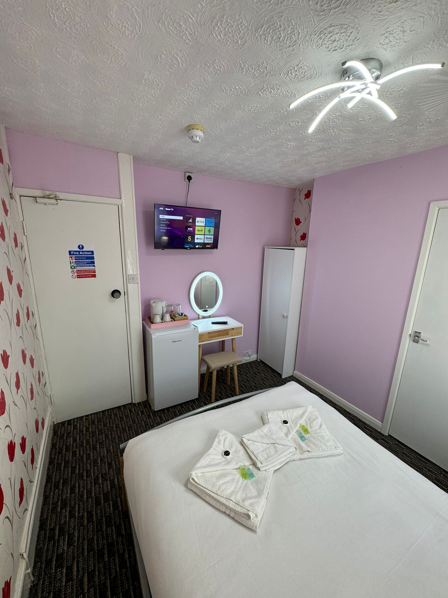 Ein Hotelzimmer mit einem Bett, einem Schreibtisch mit Spiegel, einem Fernseher und einem Kleiderschrank.