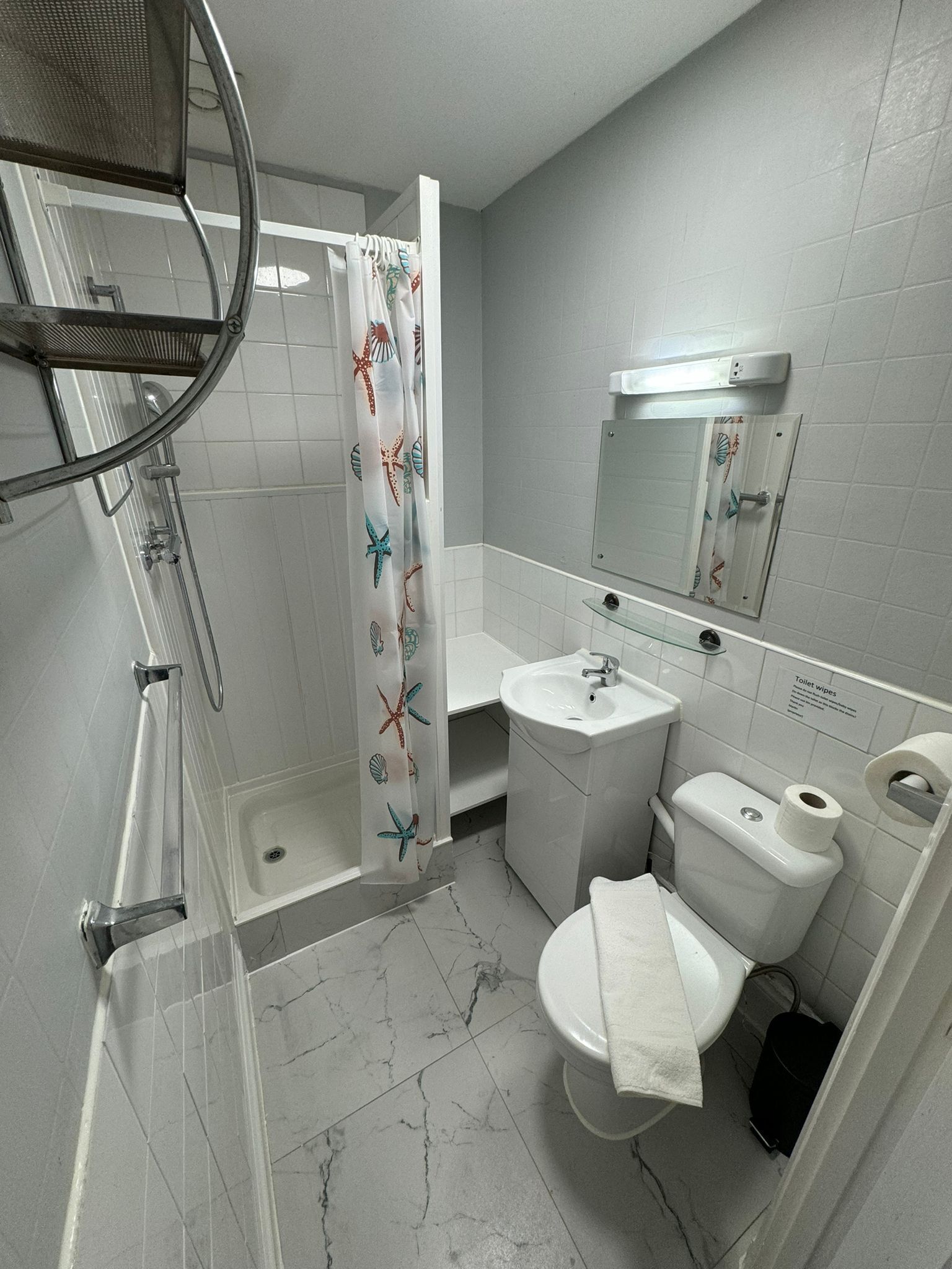 Et badeværelse med brusebad, toilet, håndvask og spejl.