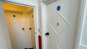 Un pasillo con puertas numeradas 5 y 7, una puerta con un letrero de 'No entrar', y una pared roja decorativa.