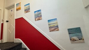 Una escalera con peldaños rojos que conduce a una puerta blanca, decorada con cuatro obras de arte con motivos playeros.