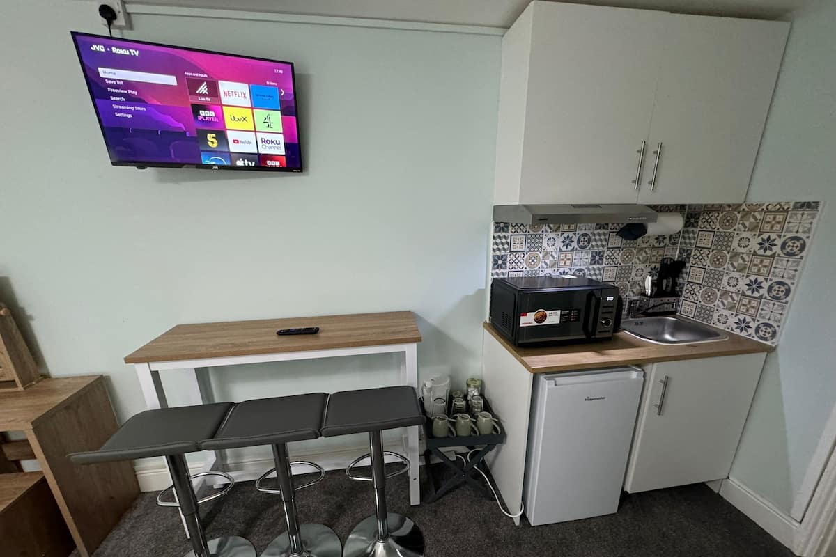 Une cuisine compacte avec un téléviseur fixé au mur qui affiche l’interface d’un service de diffusion en continu, un petit réfrigérateur, un four à micro-ondes et un évier.