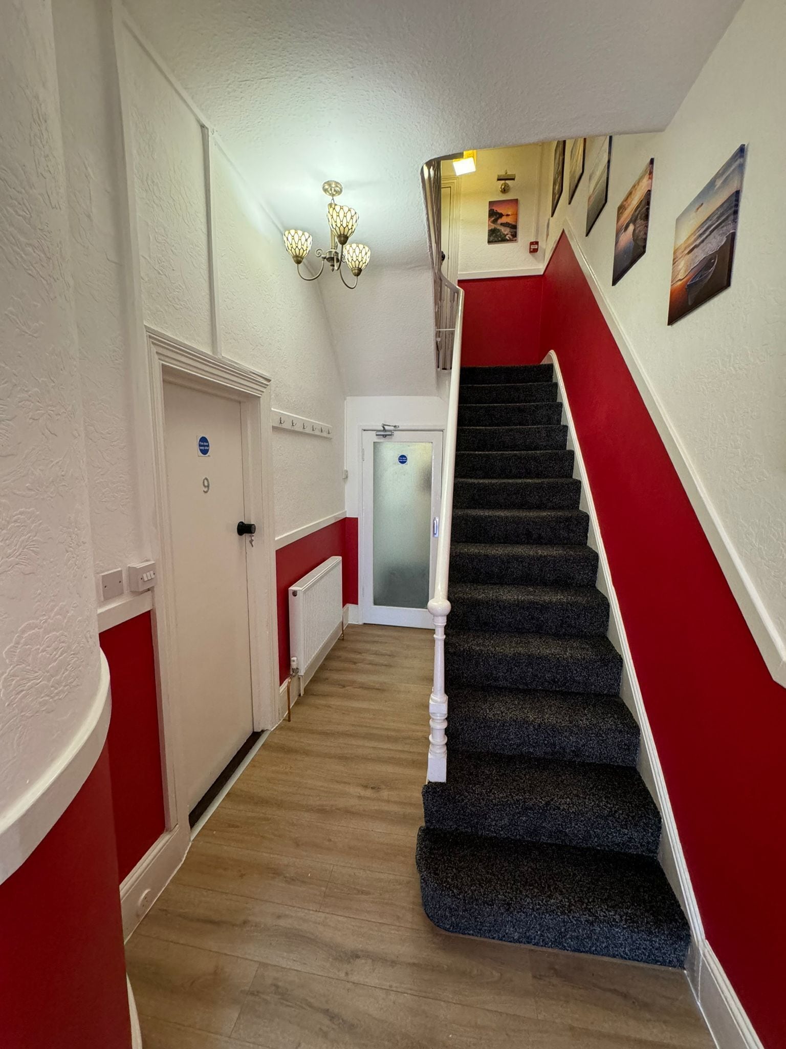 A hallway with a red and white wall, a staircase with a red handrail, and a door marked with the number 9.