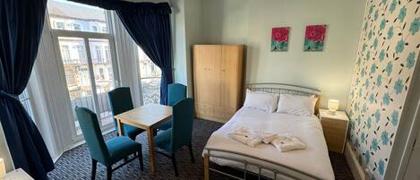 Habitación de hotel con cama, mesa con sillas, armario y vistas a la ciudad desde la ventana.