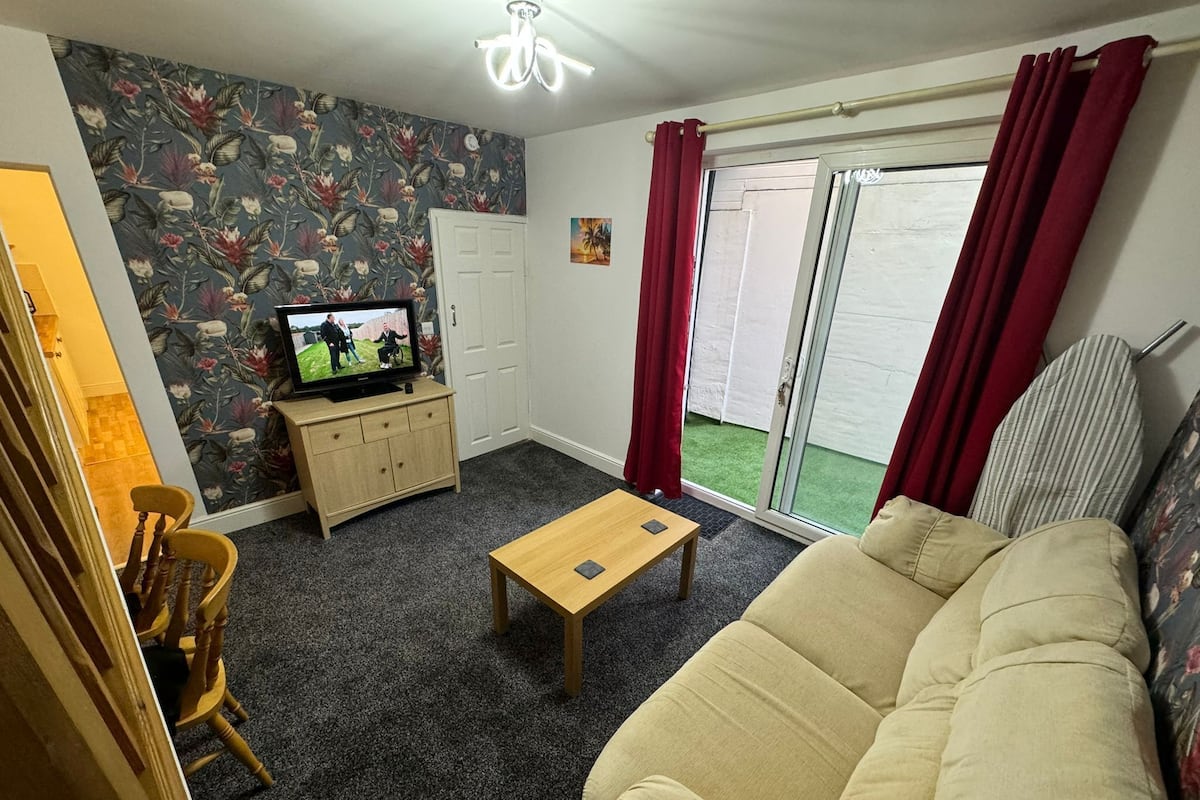 Un salon comprenant un canapé, une table basse, un téléviseur posé sur un meuble, une porte et une porte-fenêtre coulissante avec des rideaux.