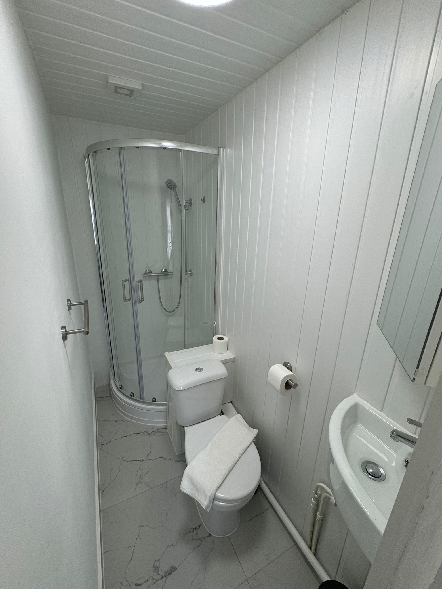 Un baño pequeño y funcional con inodoro, lavamanos y ducha con mampara de vidrio.