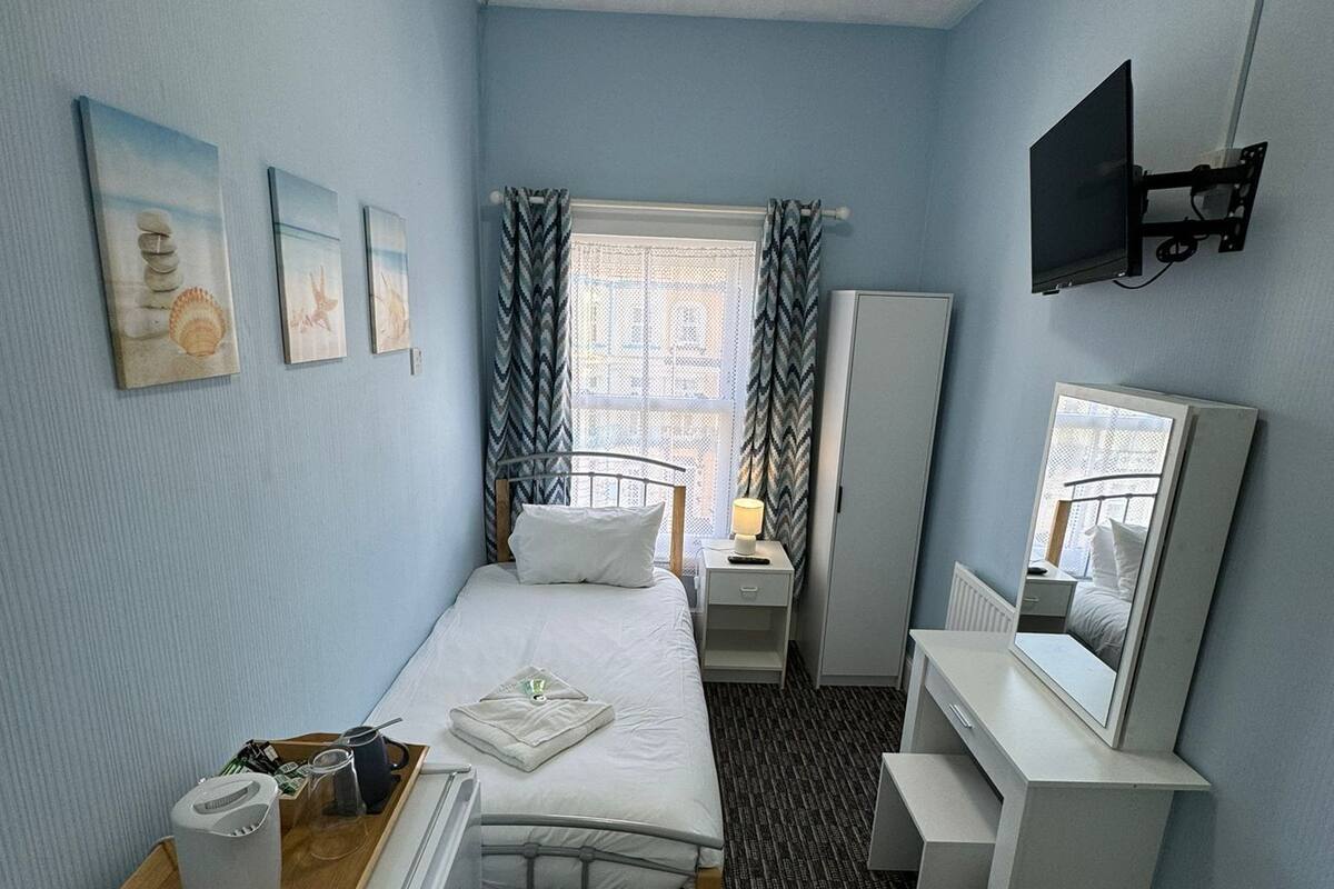 Une chambre d’hôtel de taille réduite, comprenant un lit, une table de chevet, une commode et un téléviseur fixé au mur.