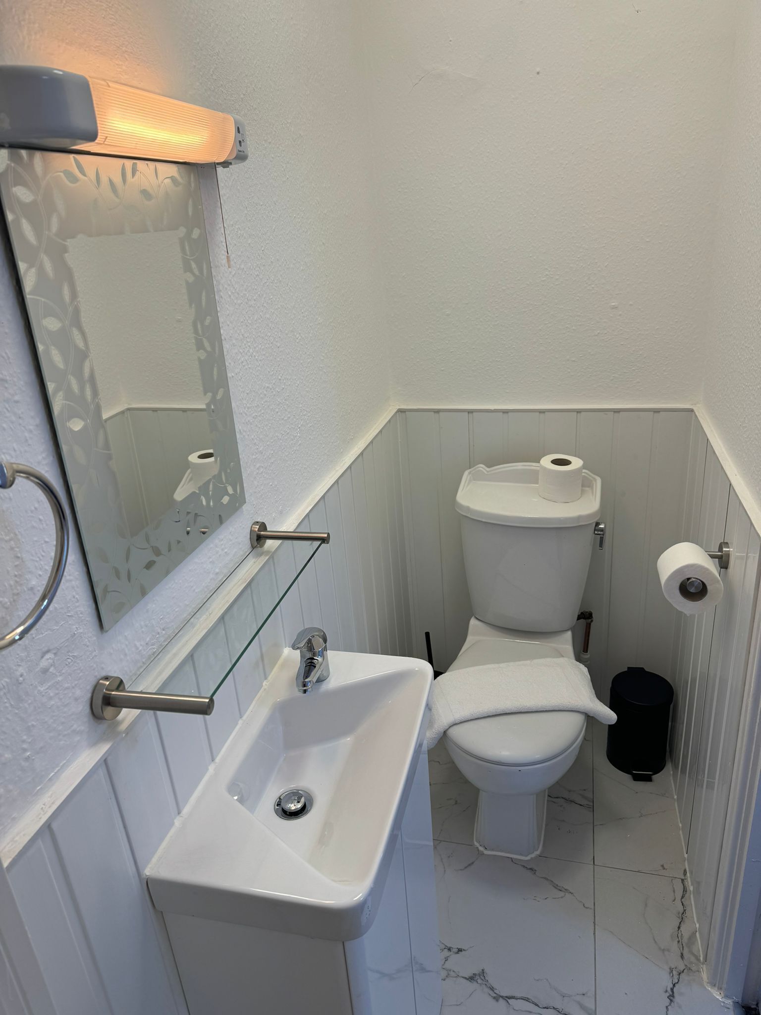 Un bany amb un lavabo blanc, un vàter i un mirall amb marc decoratiu.