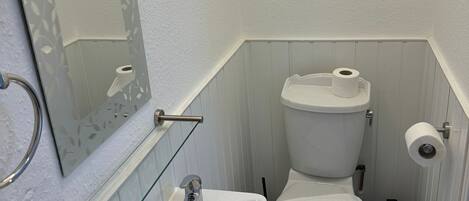 Un baño con lavamanos blanco, inodoro y espejo con marco decorativo.