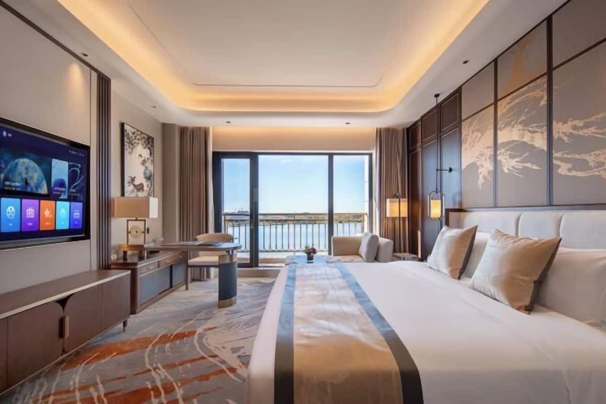 Una habitación de hotel moderna con una cama grande, un televisor, un escritorio y vistas a la ciudad.