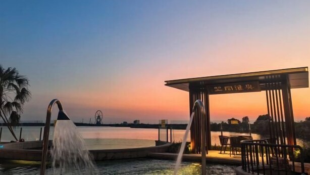 Una fuente de agua con un pabellón y zona de estar con vistas a un cuerpo de agua al atardecer.