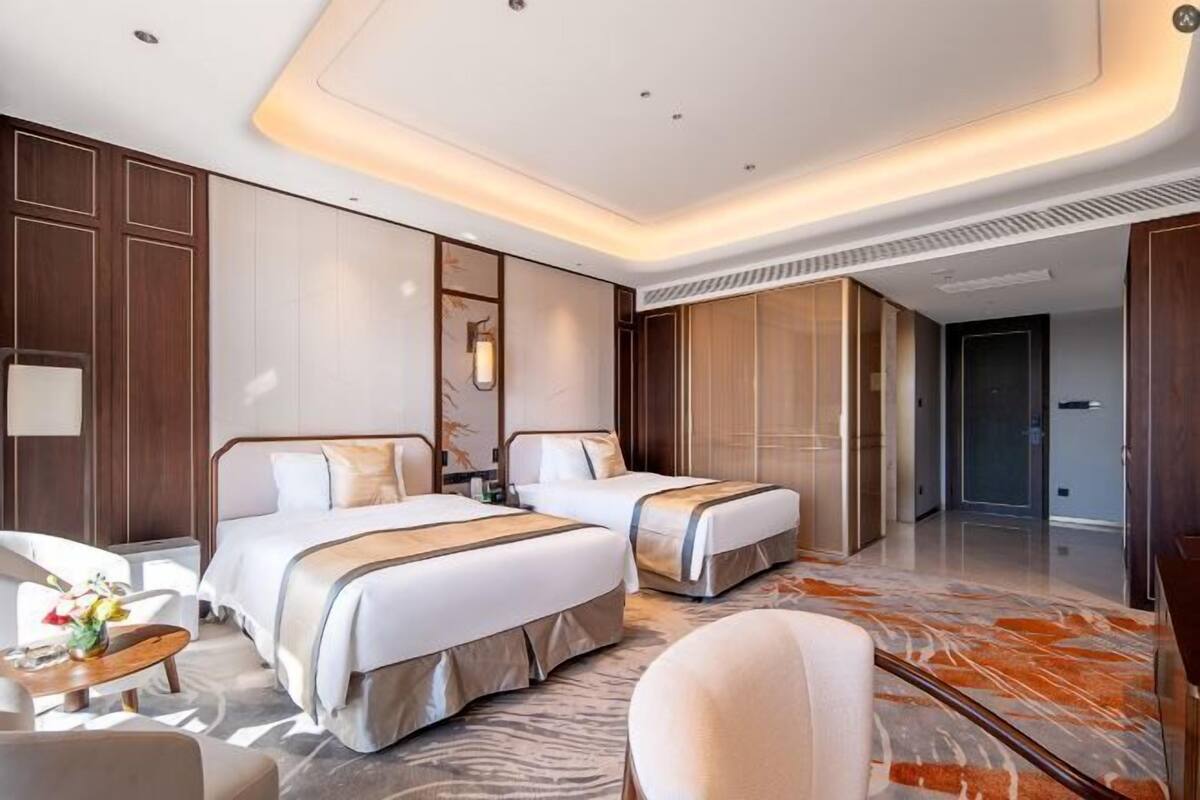 Habitación de hotel con dos camas, un área de descanso con una silla, una mesita y un espejo grande.