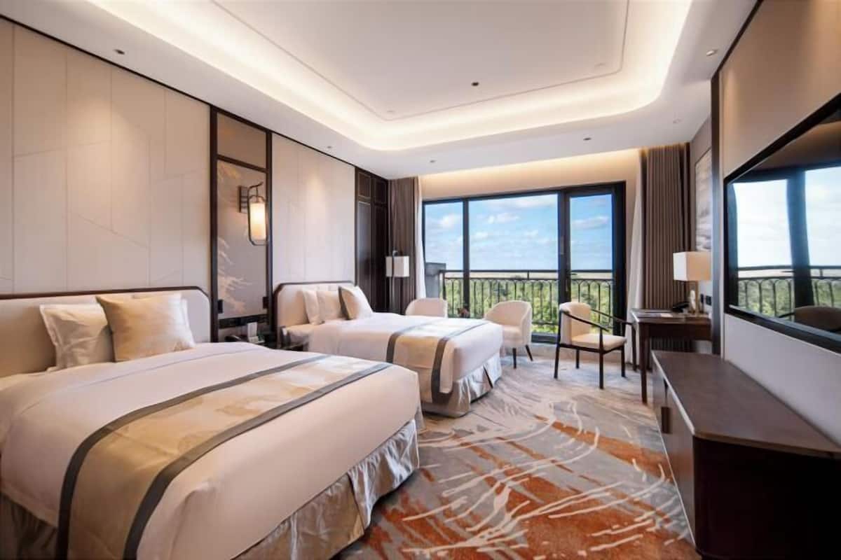 Habitación de hotel con dos camas, un escritorio, una silla, un balcón con vistas y un ventanal grande.