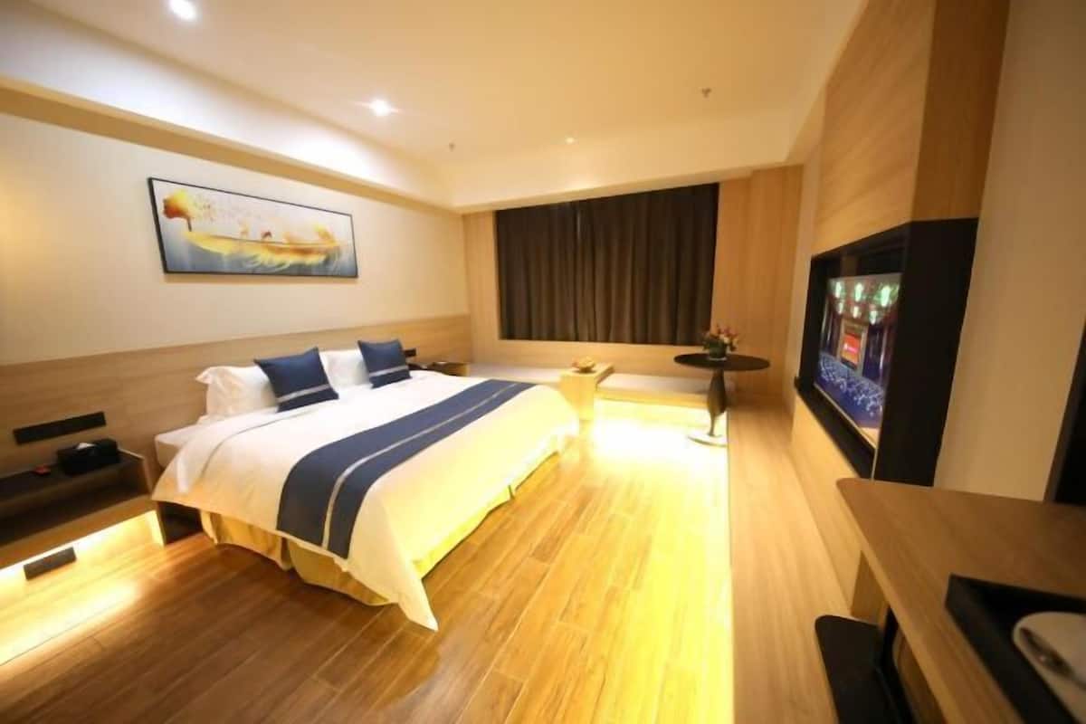 Una habitación de hotel con una cama, televisor, un cuadro y suelo de madera.