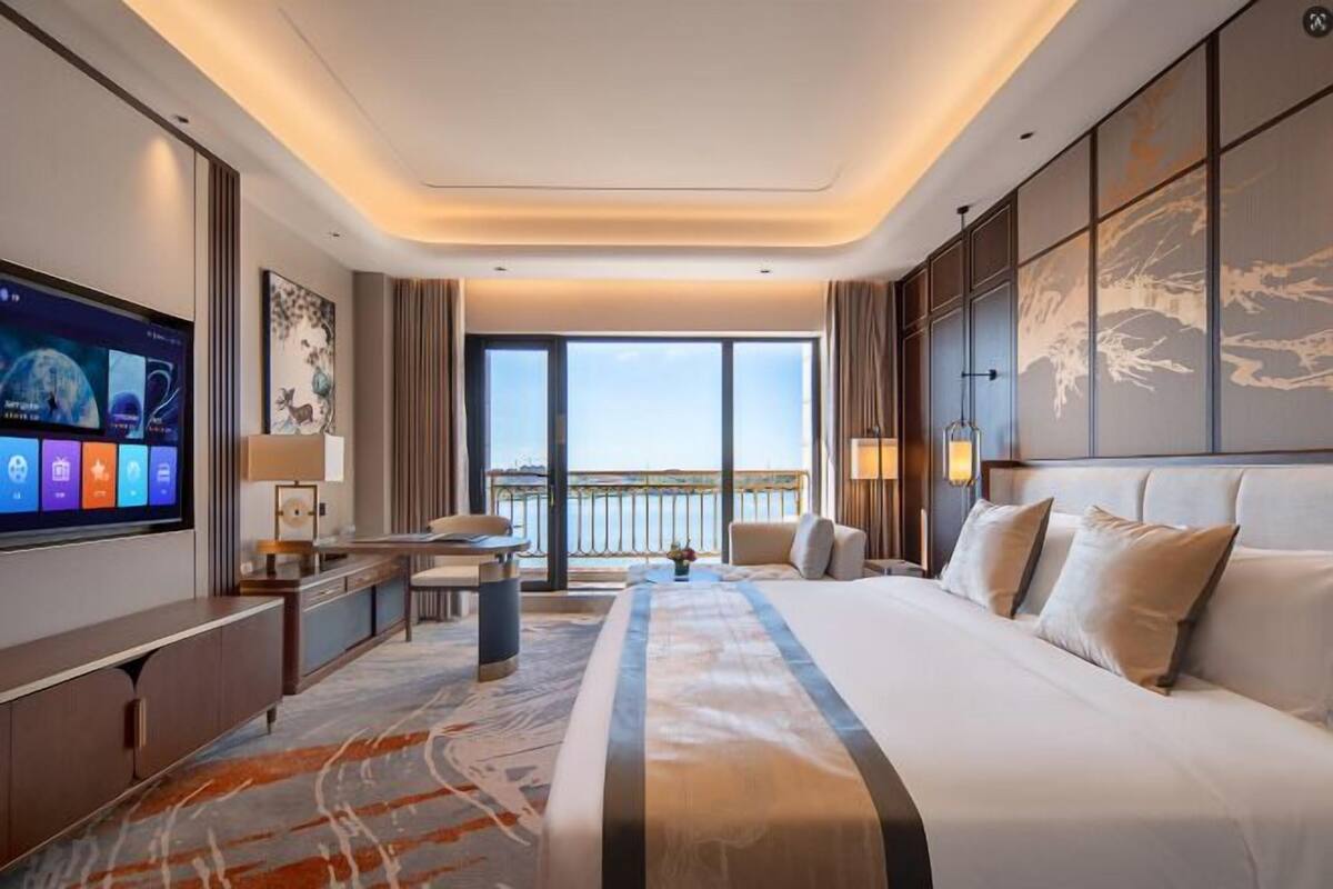 Habitación de hotel moderna con una cama grande, televisor de pantalla plana, escritorio y vista al agua.