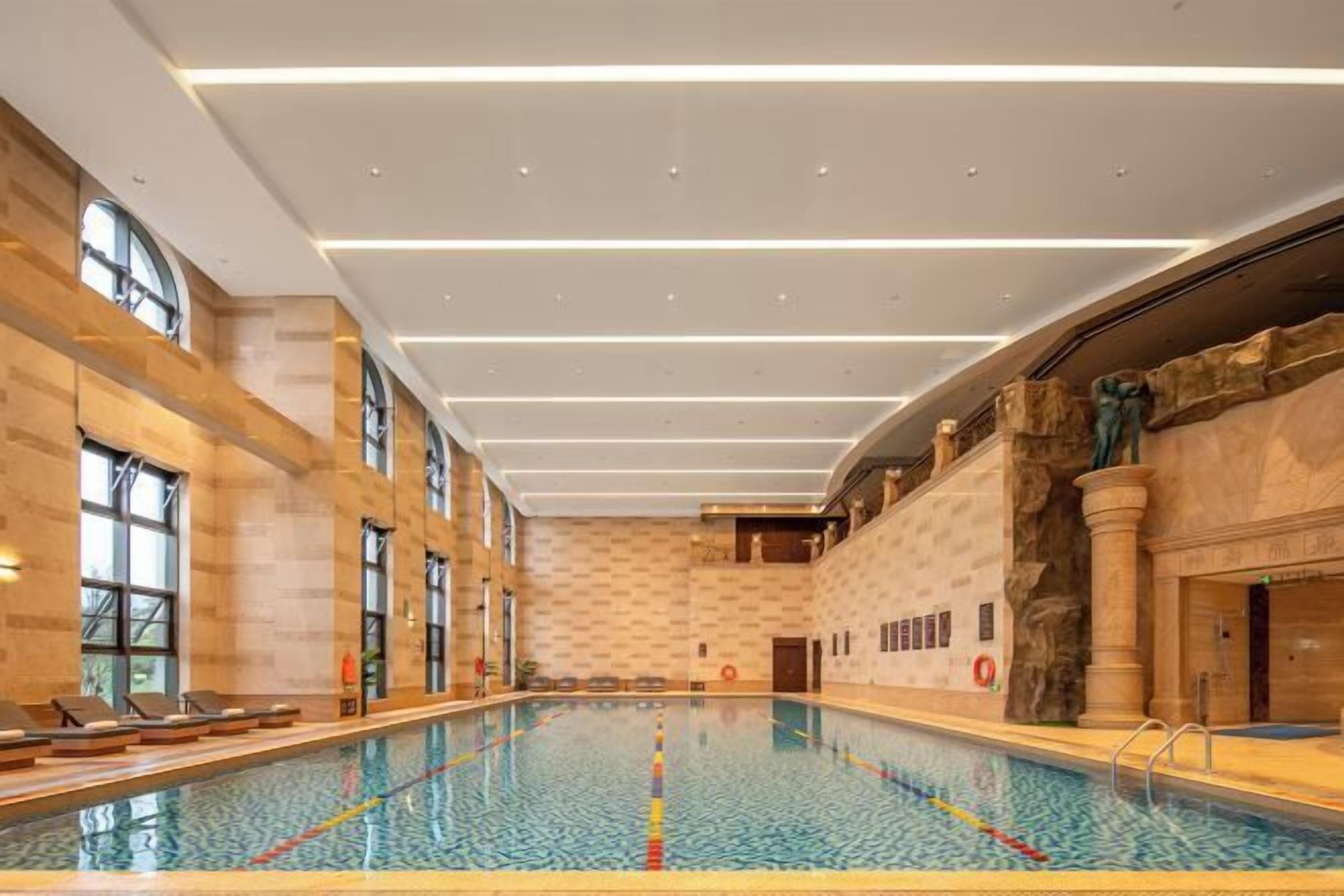 An indoor swimming pool with clear lane markings, a stone wall on one side, and a modern ceiling design.