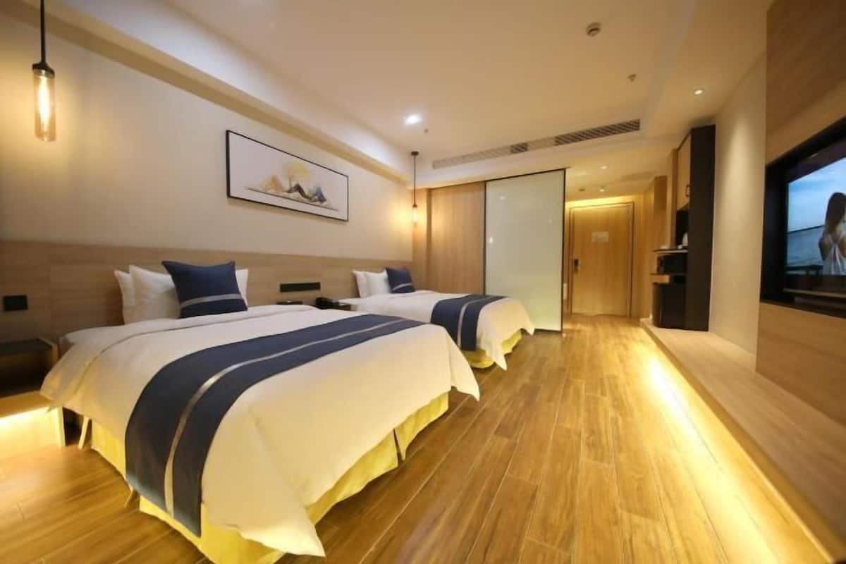 Habitación de hotel con dos camas, suelo de madera, televisión y un cuadro en la pared.