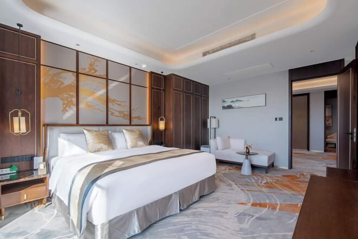 Una habitación de hotel moderna con una cama grande, zona de estar y vistas al exterior.