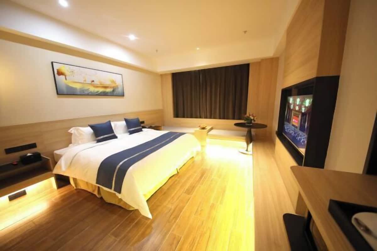 Una habitación de hotel con una cama grande, un televisor de pantalla plana, una mesita y un cuadro en la pared.