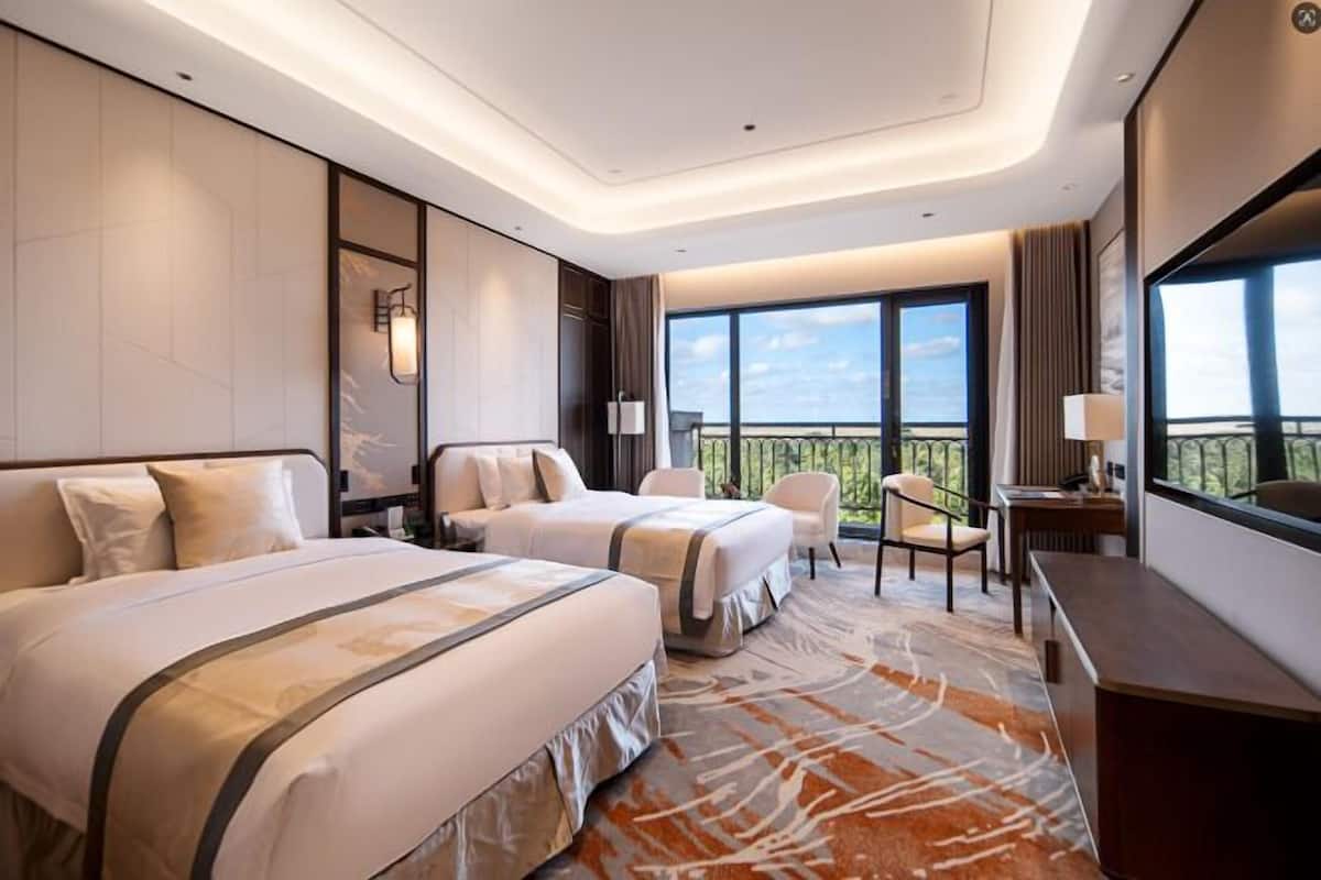 Habitación de hotel con dos camas, un escritorio, una silla y un ventanal con vistas.