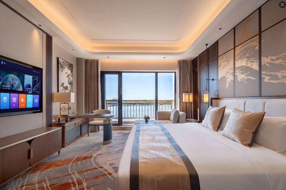 Habitación de hotel moderna con una cama grande, televisor de pantalla plana, escritorio y vista al mar.