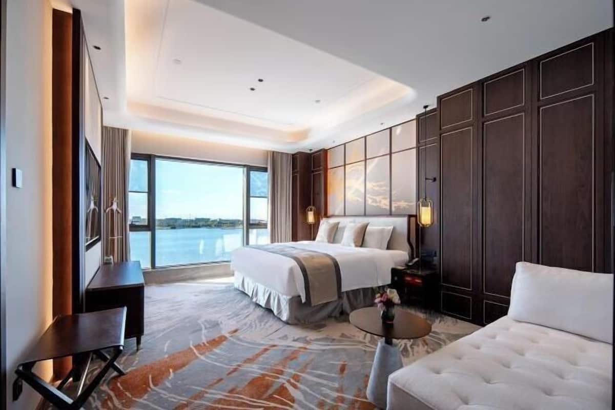Habitación de hotel moderna con una cama grande, un sofá, un escritorio y vistas al agua.