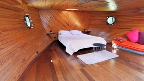 A cozy bedroom with a wooden ceiling, a bed with white bedding, a small round table, and a red sofa with pillows. - Peniche Refuge Seine (Vigneux-sur-Seine)