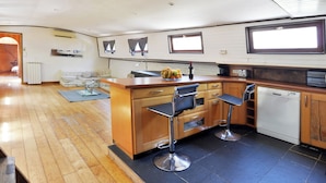 A compact kitchen with a wooden countertop, two bar stools, a dishwasher, and a small window. - Peniche Refuge Seine (Vigneux-sur-Seine)