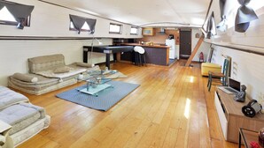 A compact living space with a kitchenette, a dining area, and a seating area with cushions and a glass coffee table. - Peniche Refuge Seine (Vigneux-sur-Seine)