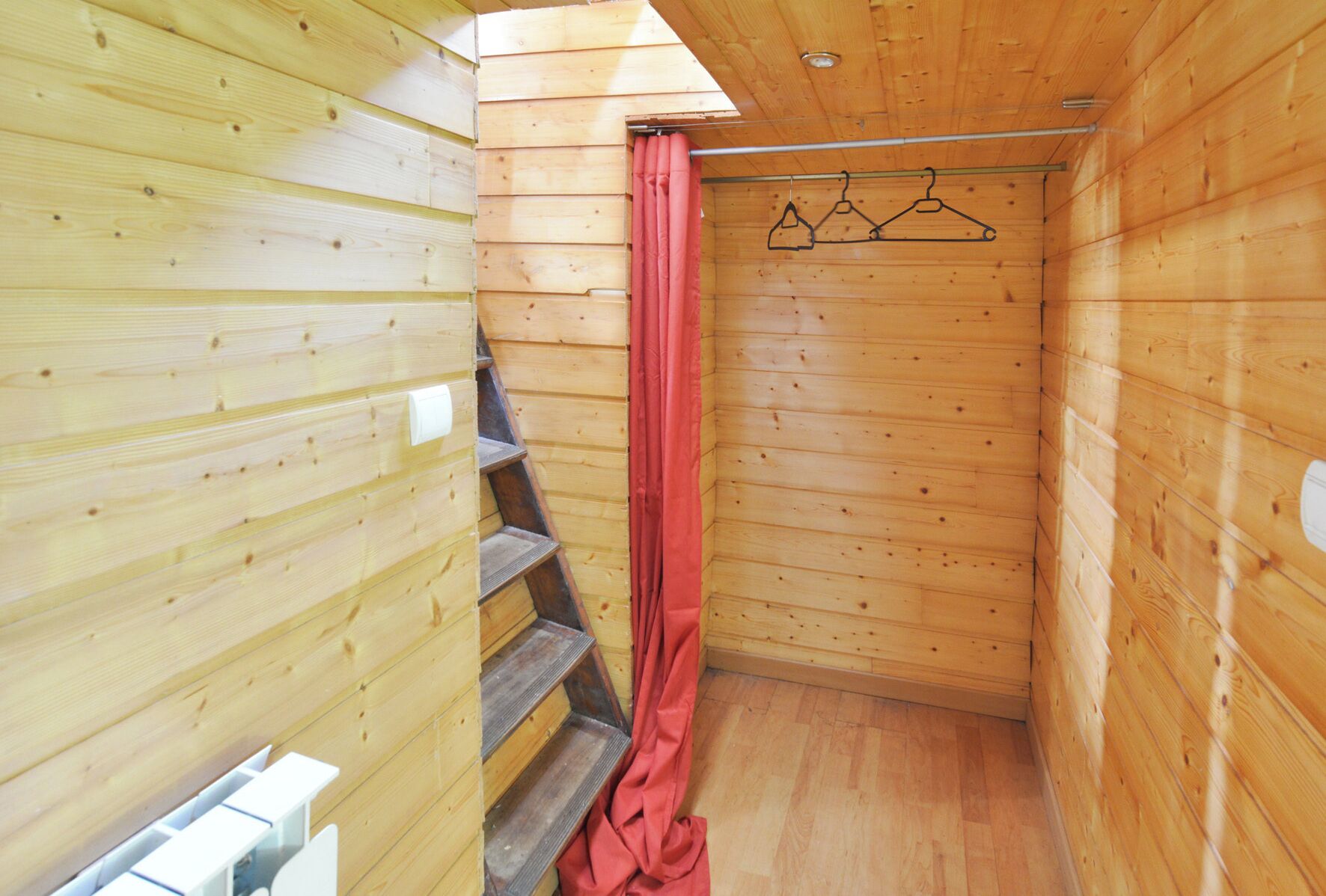 A wooden cabin with a wooden staircase, a shower curtain, and a clothesline with hangers.