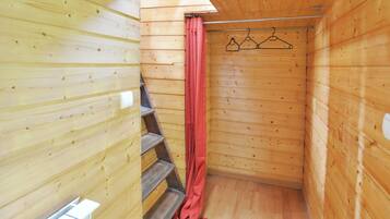 A wooden cabin with a wooden staircase, a shower curtain, and a clothesline with hangers.