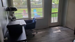 A room with a desk, chair, and large windows with blinds.
