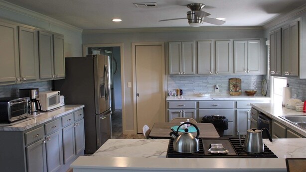 A modern kitchen with grey cabinets, a stainless steel refrigerator, a microwave, and a gas stove.