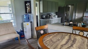 A modern kitchen with a built-in microwave, toaster, and kettle. There is a water dispenser and a refrigerator. The dining area has a round table with chairs.
